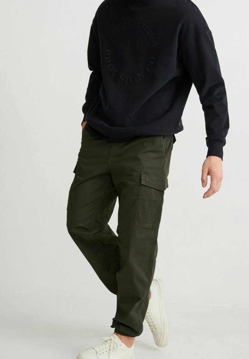 Groene cargobroek met meerdere zakken, tapered fit, gemaakt van katoen, gecombineerd met een zwarte sweatshirt en witte sneakers.