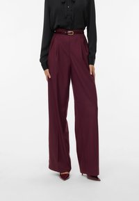 Pantaloni larghi bordeaux in un tessuto morbido con pieghe e vita alta, abbinati a una blusa nera e una cintura coordinata.