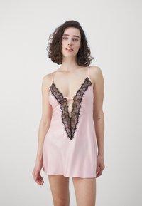 Pink satin nightdress with black lace trim, deep V-neckline, adjustable spaghetti straps, and a loose fit that falls above mid-thigh.
