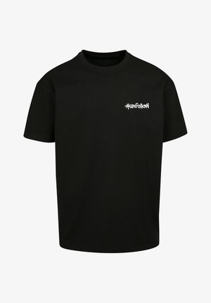 T-shirt noir oversize avec logo sur la poitrine, associé à un pantalon cargo beige avec plusieurs poches, des poignets élastiques et des baskets blanches.