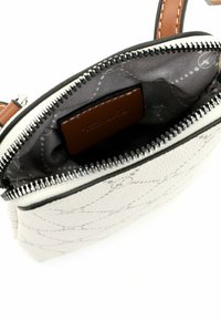 Petit sac bandoulière blanc avec une fermeture éclair noire, une poignée en cuir beige et un intérieur en tissu à motif gris avec une étiquette en cuir marron.