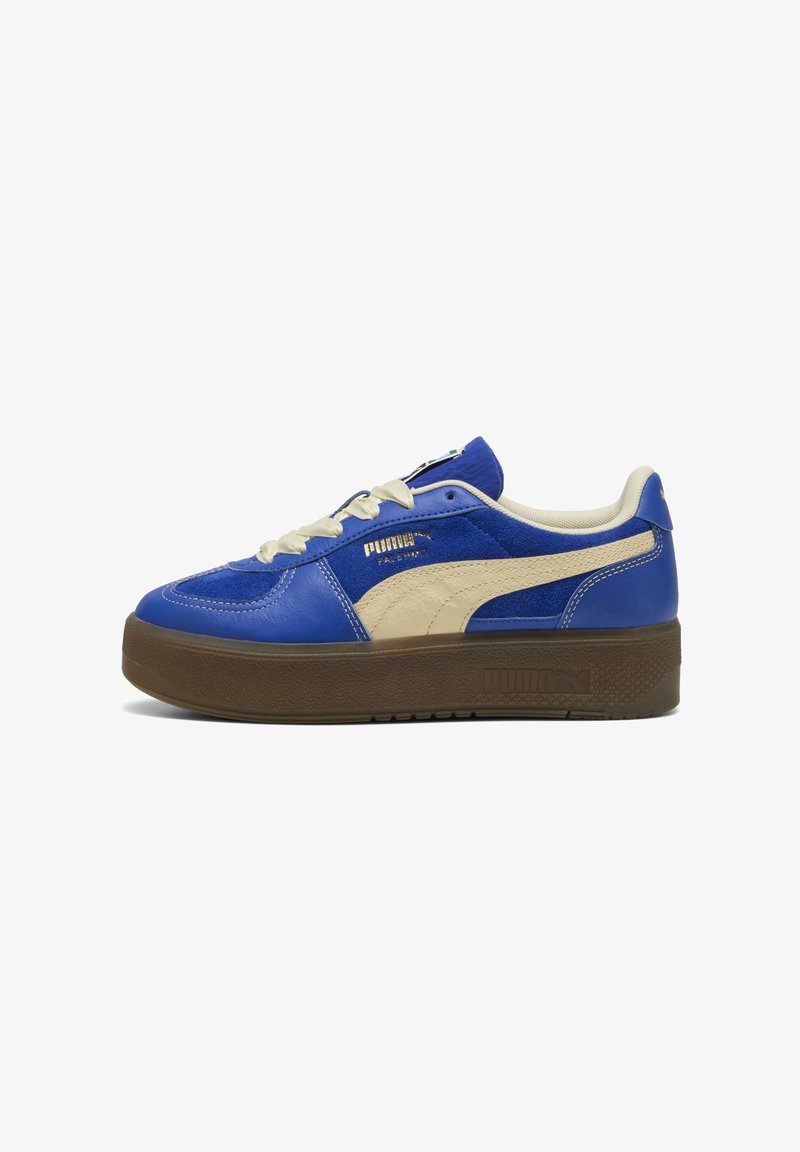 Baskets basses Puma en suède bleu et cuir avec une bande beige, des lacets crème et une semelle épaisse en caoutchouc marron, vue latérale.