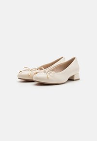 Ballerines beige à bout rond, avec un nœud décoratif et des accents dorés. En cuir souple et à talon carré bas.