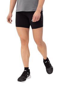 Schwarze Sportshorts mit taillierter Passform, versehen mit einem JAKO-Logo an der Seite. Kombiniert mit schwarzen Turnschuhen, die eine sportliche Ästhetik unterstreichen.
