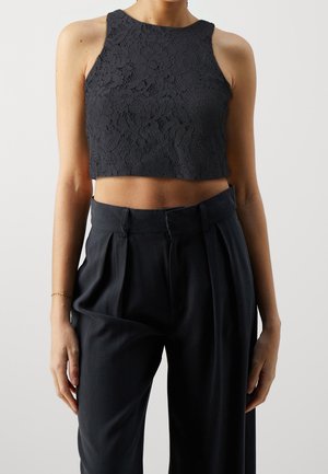 Top court en dentelle noire avec un col montant et un design sans manches, associé à un pantalon noir plissé à taille haute. Motif floral texturé.