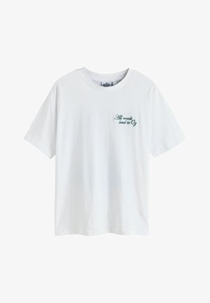 White cotton t-shirt with short sleeves, featuring green embroidered text "All roads lead to Oz" on the left side. Simple crewneck design.