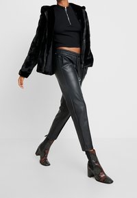 Czarna kurtka z futerkiem z sztucznego futra z kapturem, w zestawieniu z czarnymi skórzanymi spodniami ze sznurkiem ściągającym i dopasowanym krojem oraz botkami w wzór skóry węża.