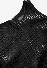 Haut en sequins noirs avec une surface texturée, doté d'un design sans manches et d'un col rond. Fermeture éclair au dos.