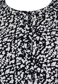 Blouse à motifs noir et blanc avec un col rond, une courte patte de boutonnage et une texture légère. Les accents présentent des taches abstraites.