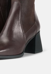 Brown leather ankle boot with a glossy finish, rounded toe, and mid-height block heel. Side elastic panel for ease of wear.
