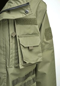 Chaqueta verde oliva con cremallera frontal, múltiples bolsillos y parches de gancho y bucle. Presenta un tejido suave y duradero, además de elementos de diseño militar.