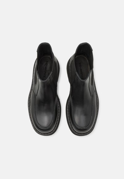 Chaussures noires à enfiler avec une tige en cuir lisse, des panneaux élastiques sur les côtés et un détail de couture contrastante le long de la semelle.