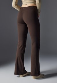 Pantalones acampanados marrones hechos de una suave tela elástica con una alta cintura. Presenta detalles de costura sutiles y aberturas laterales en el dobladillo.