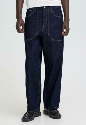 Donkerblauwe denimbroek met rechte pijpen, contrasterende witte stiksels, meerdere zakken en een comfortabele pasvorm. Taille voorzien van een knoopsluiting.