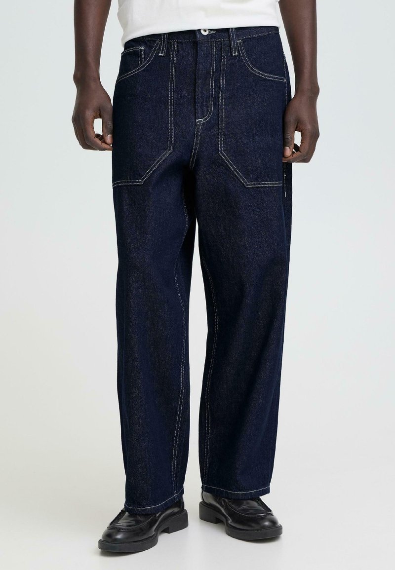 Donkerblauwe denimbroek met rechte pijpen, contrasterende witte stiksels, meerdere zakken en een comfortabele pasvorm. Taille voorzien van een knoopsluiting.
