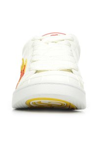 Fehér sneaker, textúrázott bőrrel, narancssárga és sárga láng hímzéssel az oldalán, és szőtt fűzőkkel a párnázott nyelv felett.
