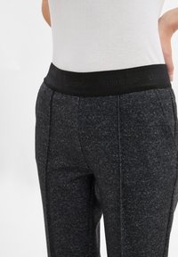 Schwarzer elastischer Bund mit geprägtem Branding auf grauen strukturierten Stoffhosen, die ein tailliertes Design und eine glatte Oberfläche aufweisen.