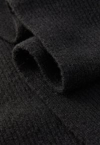 Tissu noir avec une surface douce et texturée, présentant une finition légèrement duveteuse et un subtil motif côtelé. Enroulé en plis lâches.