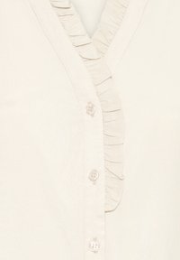 Cremefarbenes Bluse mit vertikaler Rüsche entlang des knöpfbaren V-Ausschnitts, ausgestattet mit drei kleinen, durchsichtigen Knöpfen.