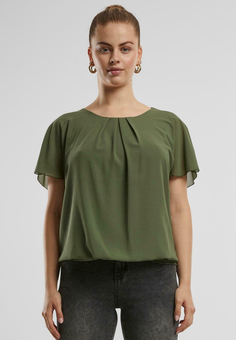 Grüne kurzärmelige Bluse aus leichtem Stoff, mit Rundhalsausschnitt und plissierter Vorderseite. Kombiniert mit dunkelgrauen Jeans.