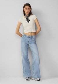 Kerman lyhythihainen crop-top, joka on yhdistetty vaaleansinisiin korkeavyötäröisiin leveälahkeisiin farkkuihin. Musta kuvioitu huivi korostaa asua. Hopeiset lenkkarit mukana.