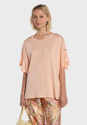 Femme portant un haut ample couleur pêche avec des manches volantées, un pantalon à motifs cachemire, tenant un sac à main jaune clair.