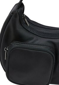 Svart stoff skulderveske med en buet design, glidedeler, og en teksturert finish. Akkompagnert av blanke hardware-detaljer.