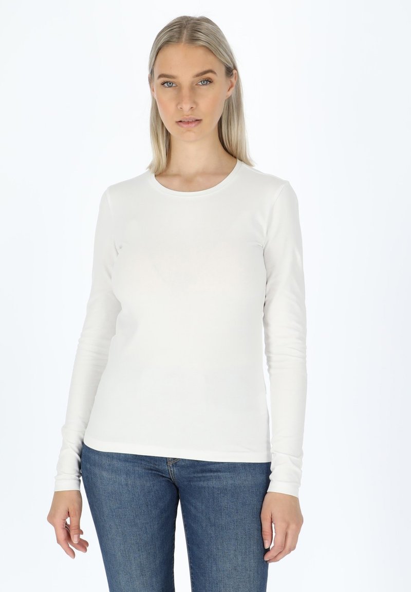 T-shirt bianco a maniche lunghe realizzato in tessuto morbido e elasticizzato con scollatura rotonda. Indossato con jeans blu, con maniche aderenti.