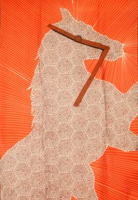 Arazzo in tessuto con una grande silhouette con spirali bianche su sfondo nero, posto su uno sfondo arancione con linee radiali.