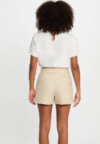 Hvit topp med korte ermer og nøkkelhull bak, sammen med beige shorts med hundetannmønster. Outfiten har en avslappet passform og teksturert stoff.