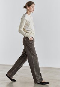 Light sweater with diagonal black lines paired with dark brown wide-leg jeans and black flat shoes on a smooth surface.