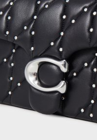 Czarna pikowana torebka z srebnym okuciem i małymi, opalizującymi ćwiekami. Posiada wyraźny srebrny zamek oraz teksturowane wykończenie ze skóry.