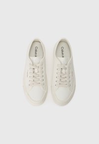 Un paio di sneakers basse off-white di Calvin Klein con lacci, con marchio sulle sole interne e sulle etichette laterali, esposte su uno sfondo bianco.