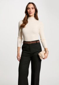 Maglione a collo alto a coste crema, pantaloni neri a gamba larga, cintura leopardata, pochette beige, accenti di gioielli in argento.