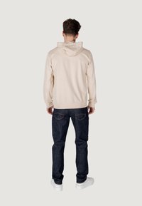 Felpa beige con cappuccio regolabile, polsini e orlo color crema, abbinata a jeans scuri e sneakers bianche. Vista posteriore dell'outfit.