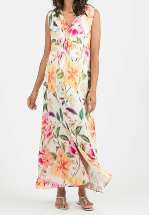 Robe maxi sans manches avec décolleté en V et imprimé floral aux tons orange, rose, vert et jaune, portée avec des sandales argentées ornées de bijoux.