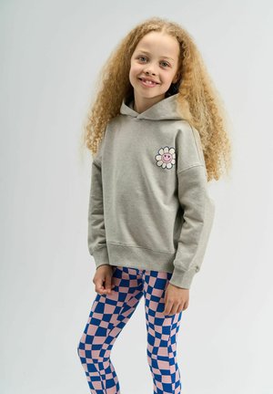 Szürke kapucnis felső virág grafikával a mellkason, rózsaszín és kék kockás leggingssel párosítva. Puha anyag, laza szabás és hosszú ujjú.