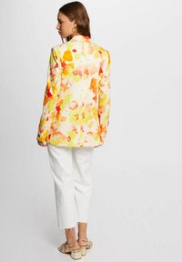 Blazer floral en crema con patrones en naranja y amarillo, combinado con pantalones cortos blancos y sandalias de tacón beige. Textura de tela suave.