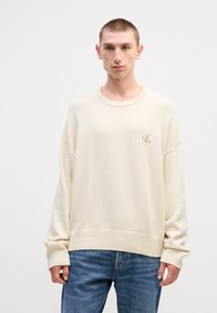 Κρέμα φούτερ μακρύ μανίκι με ριμπ μανσέτες και κάτω στρίφωμα. Διαθέτει ένα μικρό κεντημένο λογότυπο στο στήθος. Συνδυάζεται με μπλε τζιν.