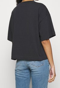 Sort oversized bomulds t-shirt med korte ærmer. Afslappet design, firkantet form, ufuldstændig kant. Båret med lyseblå denim jeans.