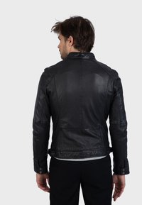 Čierna kožená bunda s priliehavým strihom, viditeľnými švovými detailmi a manžetami na cvoky. Hladká textúra a krátky golier.