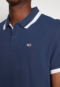 Polo marine en tissu texturé avec un col blanc contrastant, une patte de boutonnage à trois boutons et un petit logo brodé sur la poitrine.