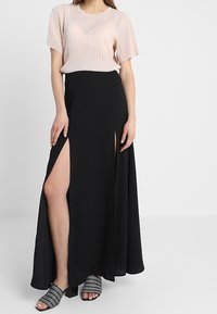 Světle růžový skládací top v kombinaci s černou maxi sukni s postranními rozparky. Modelka nosí černobílé vzorované lodičky.