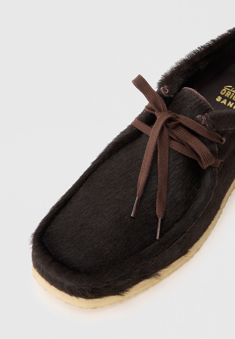 Brown fur-covered shoe with a rounded toe, secured by a dark brown lace. Soft texture with a beige rubber sole.