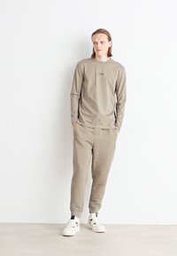 Blusa de manga longa cinza clara e calças de treino combinando com uma impressão de logótipo subtil; apresenta um tecido suave e liso e um corte descontraído, acompanhadas por ténis brancos.