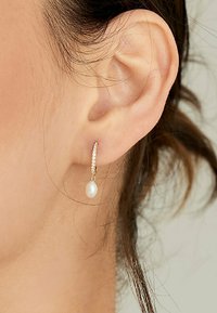 Orecchino a cerchio dorato con piccola goccia di perla bianca, decorato con gemme trasparenti lungo la parte superiore per un tocco di eleganza in più. Design semplice ed elegante.