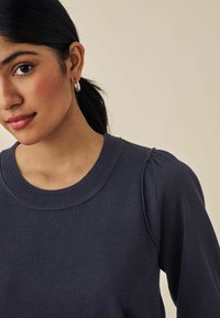 Maglione blu navy con collo a girocollo a coste e maniche a sbuffo, caratterizzato da una texture liscia e dettagli di cucitura delicati sulle spalle.