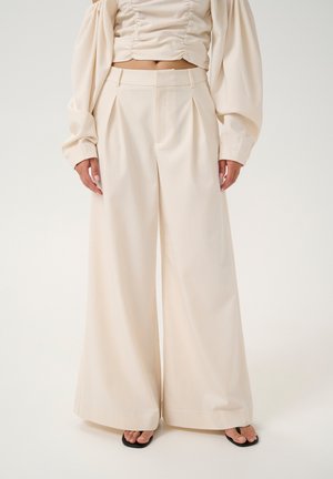 Beige wide-leg trousers with a high waist, pleats, and smooth texture, paired with a matching top featuring gathered accents.