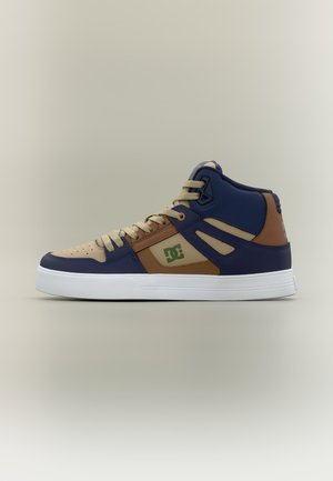 Basket montante bleu marine, beige et marron avec lacets beiges, logo vert sur le côté et semelle en caoutchouc blanche.