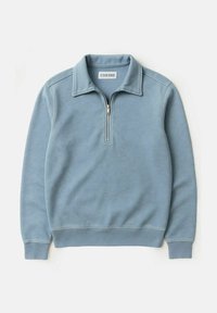 Hellblauer Halbzip-Pullover mit Stehkragen und gerippten Bündchen und Saum, flach auf einem weißen Hintergrund ausgelegt.